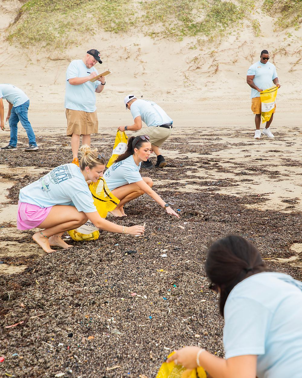 Three volunteers crouched in the seaweed line, picking up litter by hand